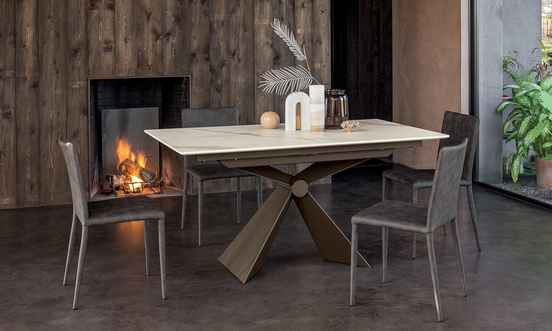 Photo d'une table rectangulaire. Pied central en V en métal bronze. Table avec plateau céramique blanc veine jaune et marron.